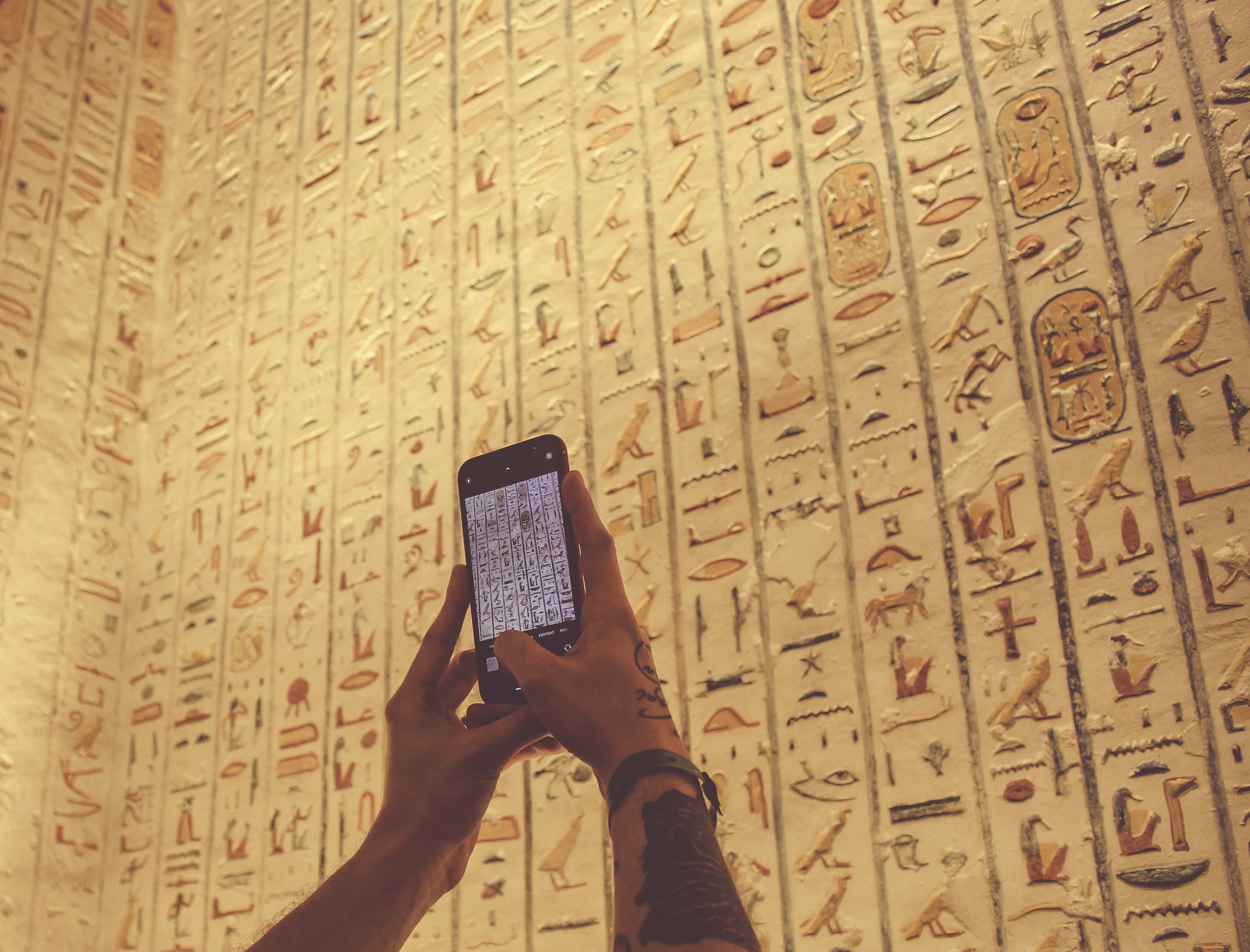 A person using a cell phone in front of a wall with egyptian writing